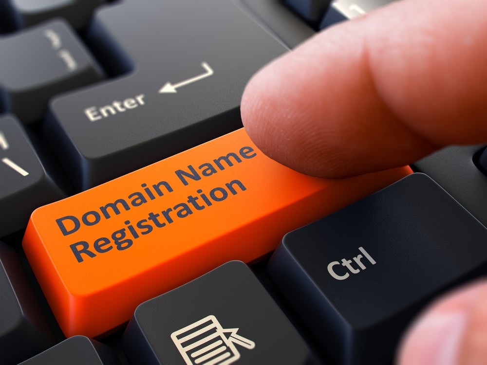 pirštu paspaudžiamas klaviatūros klavišas su užrašu "Domeno vardo registracija".