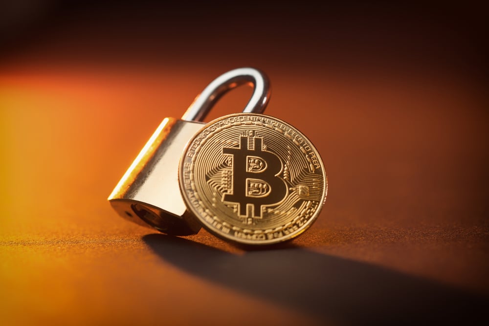 Gold coin with the Bitcoin logo on it leaning on a padlock. Represents secure cryptocurrency.